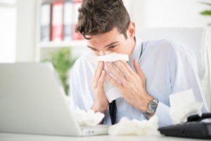 Man at desk blowing nose in tissue: MaxFilings Business Management Blog